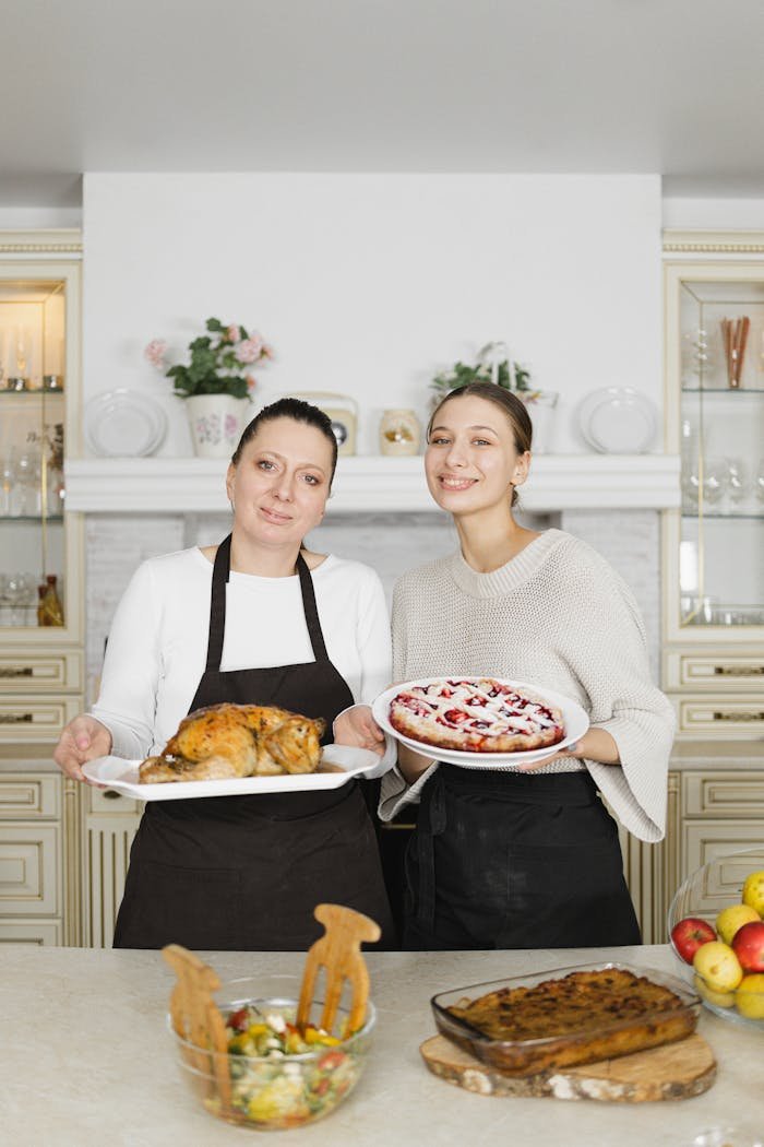 A mother and daughter happily showcasing homemade dishes in a cozy kitchen setting.