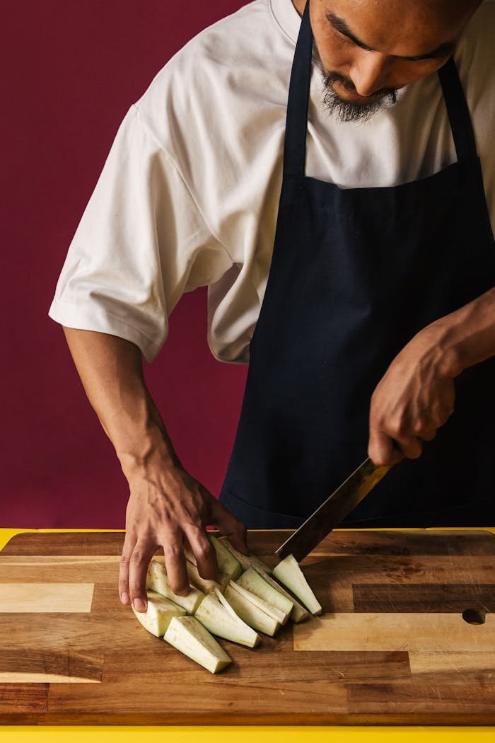 A chef expertly slices fresh eggplant on a wooden board, showcasing food preparation skills.